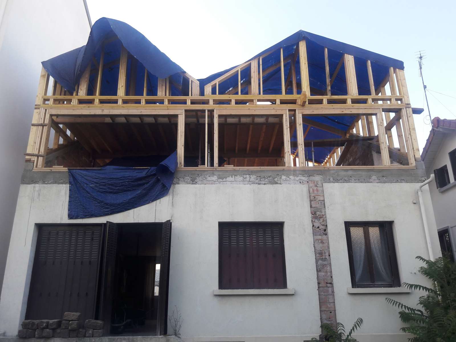La charpente des deux pignons en chantier, bâches bleues